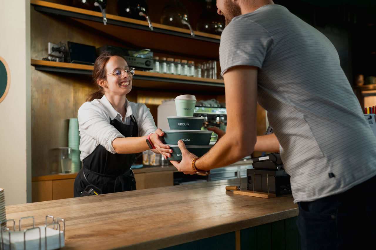 Een RECUP beker en een RECUP bowl worden in een restaurant over de toonbank aangereikt.
